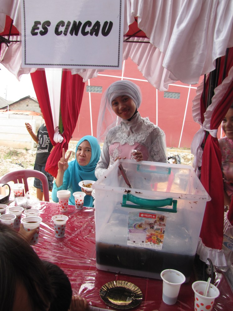 Es Cincau is a dark brown drink that has ice and mysterious, wiggling brown jelly strands. It tastes like it might be a distant relative of chocolate but it is hard to say for sure. Lya, wearing a blue hijab and a friend of Caitlin and I, is helping serve up cup after cup of Es Cincau.